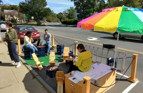 人们在街上的便携式公园里放松，在雨伞下，被游戏包围